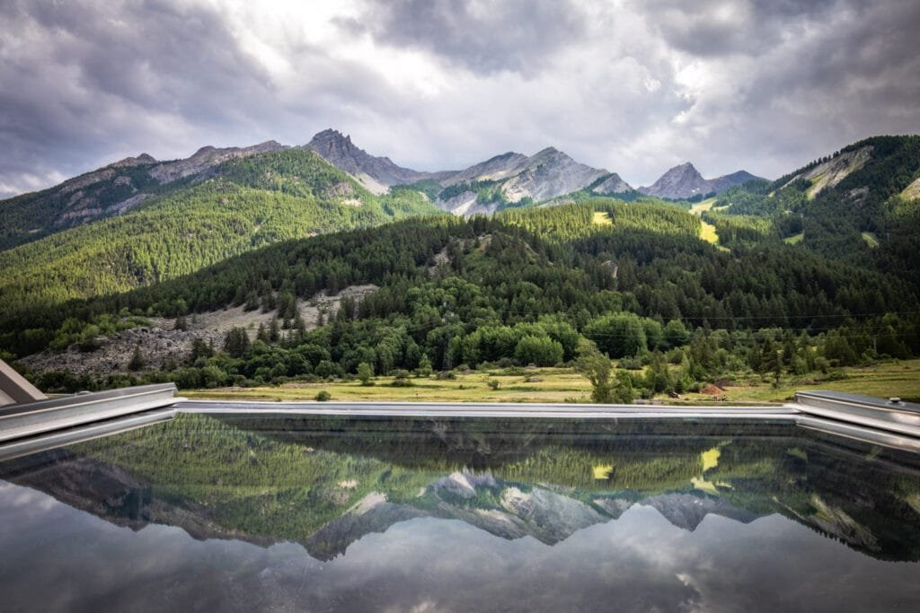 Fenêtre ouverte sur les sommet alpins se reflétant dans la vitre.