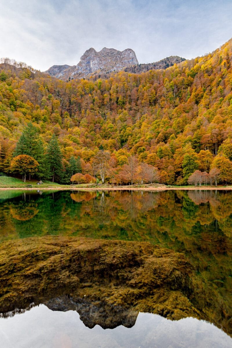 Obtenez le tirage "Lac ardent des Pyrénées" d'un lac de montagne reflétant les couleurs d'automne de la forêt sur les pentes de la montagne le surplombant