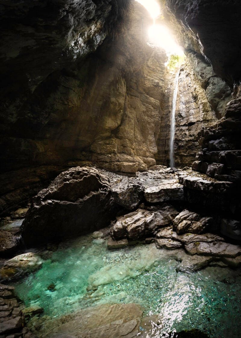 Tirage d'Art "Souterrain de vie" d'une cascade entrant dans un caverne créant un petit lac souterrain aux couleurs vives