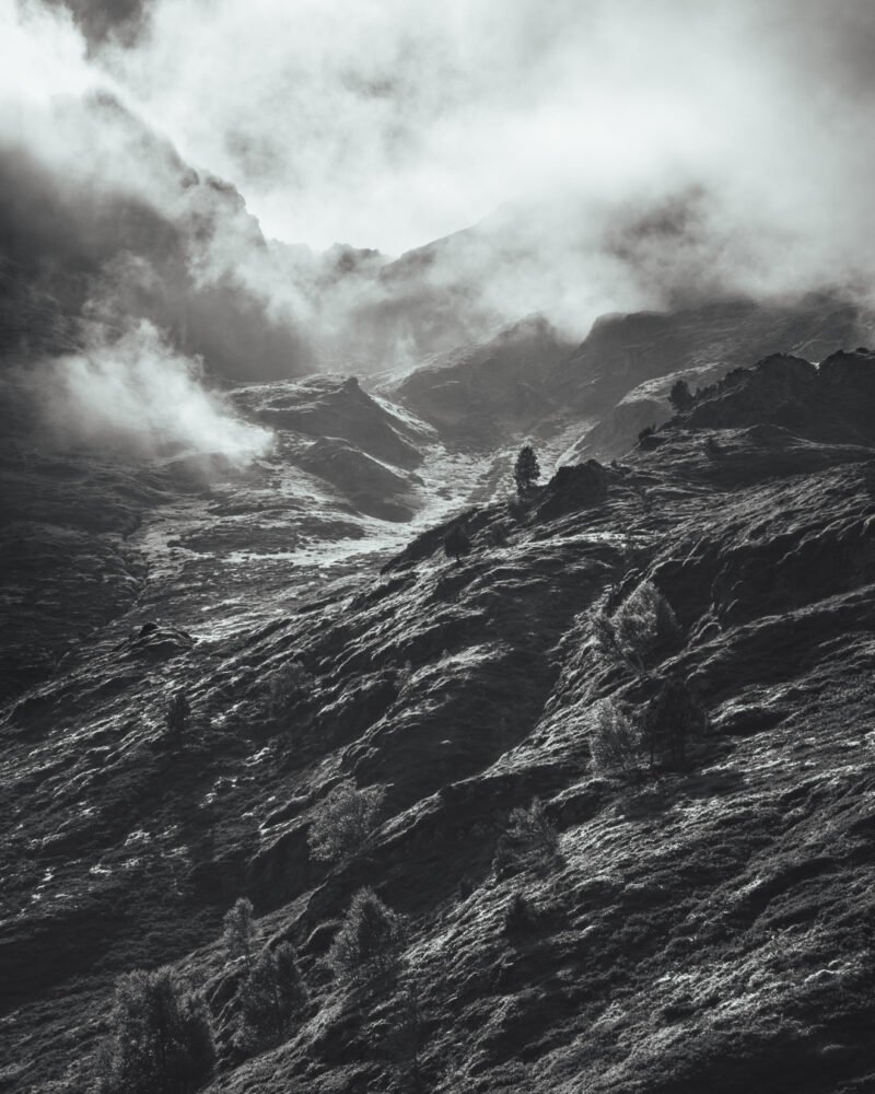 Tirage d'Art "Rayon de contraste" - Magnifique photo noir et blanc avec légères teintes bleutées d'un flanc de montagne. Le soleil éclaire d'une lumière rasante les reliefs et les quelques arbres clairsemés.